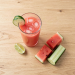 Glass of watermelon cucumber juice with ice, thin cucumber slices on the rim and a lime wedge