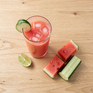 Glass of watermelon cucumber juice with ice, thin cucumber slices on the rim and a lime wedge